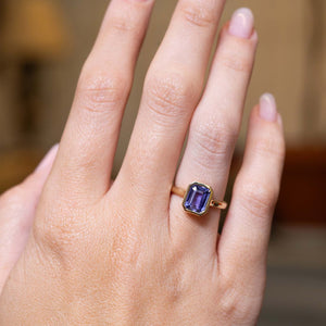 Indigo blue sapphire solitaire ring showcased on the hand in an antique-inspired yellow gold setting.