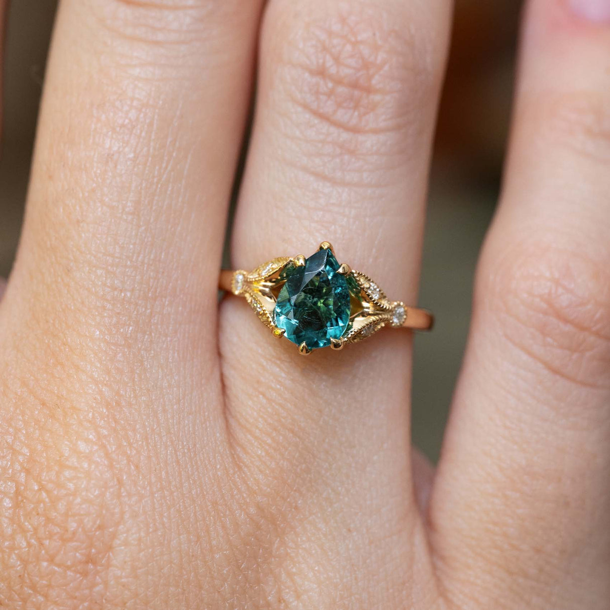 Close-up of the vintage-inspired teal tourmaline engagement ring on the finger