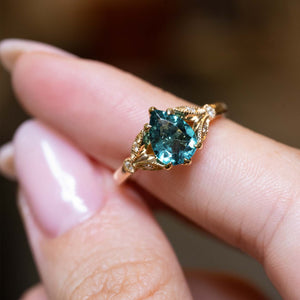Close-up of a teal tourmaline and diamond engagement ring held on the finger