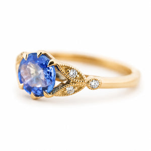 A three-quarter angle of a yellow gold engagement ring with a round blue sapphire with diamond details in the shoulders.