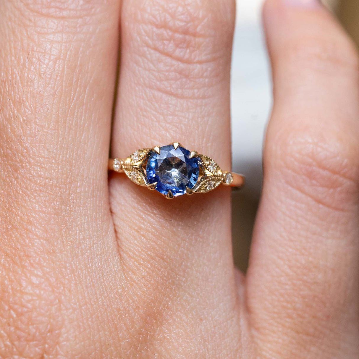 Vintage-inspired blue-purple sapphire and diamond engagement ring in yellow gold worn on the finger.