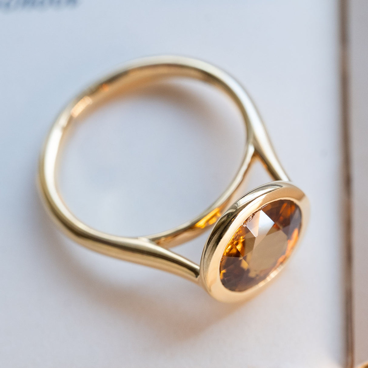 An antique-inspired, deep orange zircon solitaire ring in yellow gold showing it's rub-over setting. 
