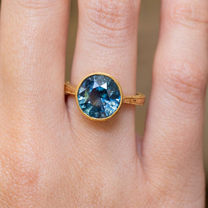 An antique-inspired, Caribbean blue-green sapphire solitaire ring in yellow gold.
