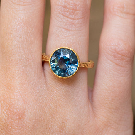 An antique-inspired, Caribbean blue-green sapphire solitaire ring in yellow gold.