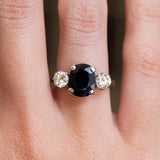 A close-up of a hand wearing a vintage white gold midnight-blue sapphire and diamond three-stone ring.