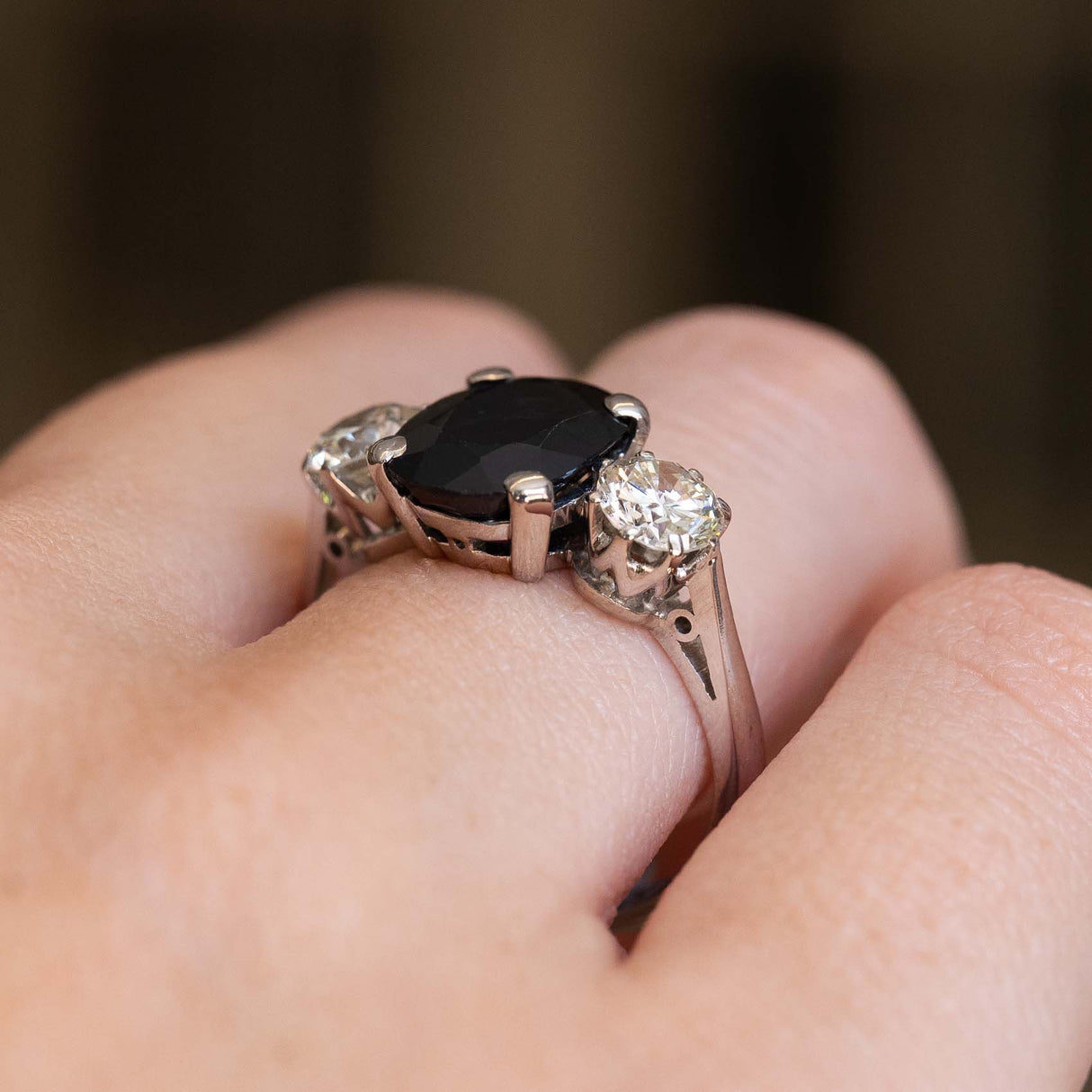 A close-up of a white gold ring with a large dark blue sapphire flanked by a round diamond on either side.