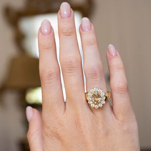 Vintage 1980s fancy coloured brown diamond cluster cocktail ring worn on the hand, featuring an oval brown diamond surrounded by brilliant-cut white diamonds in yellow gold.
