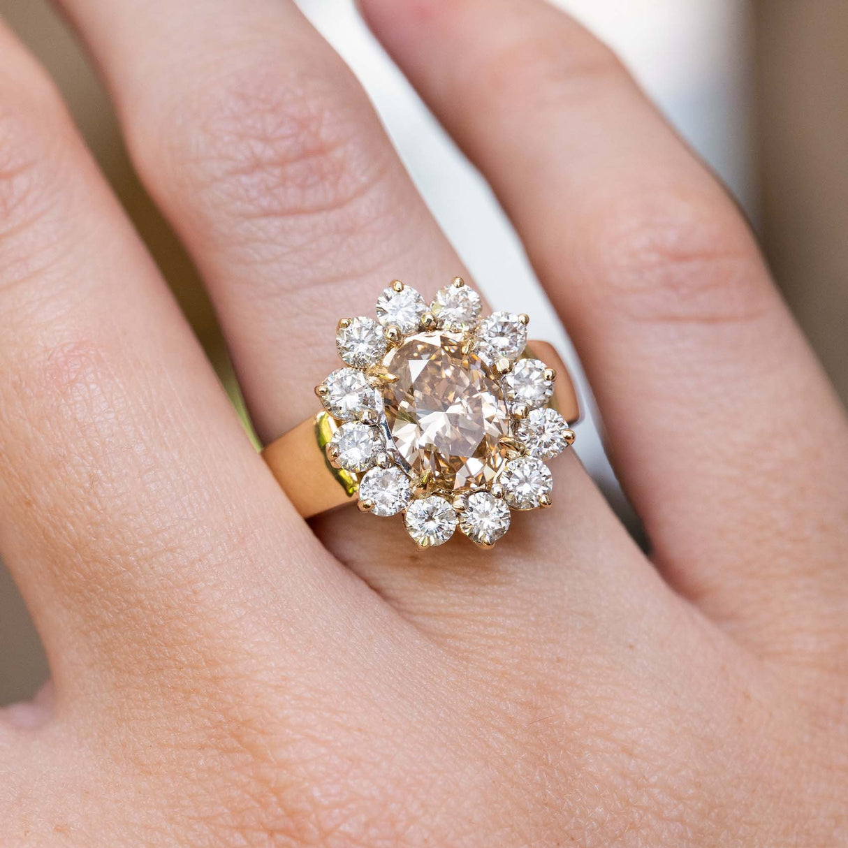 Close-up of a vintage fancy coloured brown diamond cluster cocktail ring on the finger, showcasing an oval brown diamond encircled by brilliant-cut diamonds.