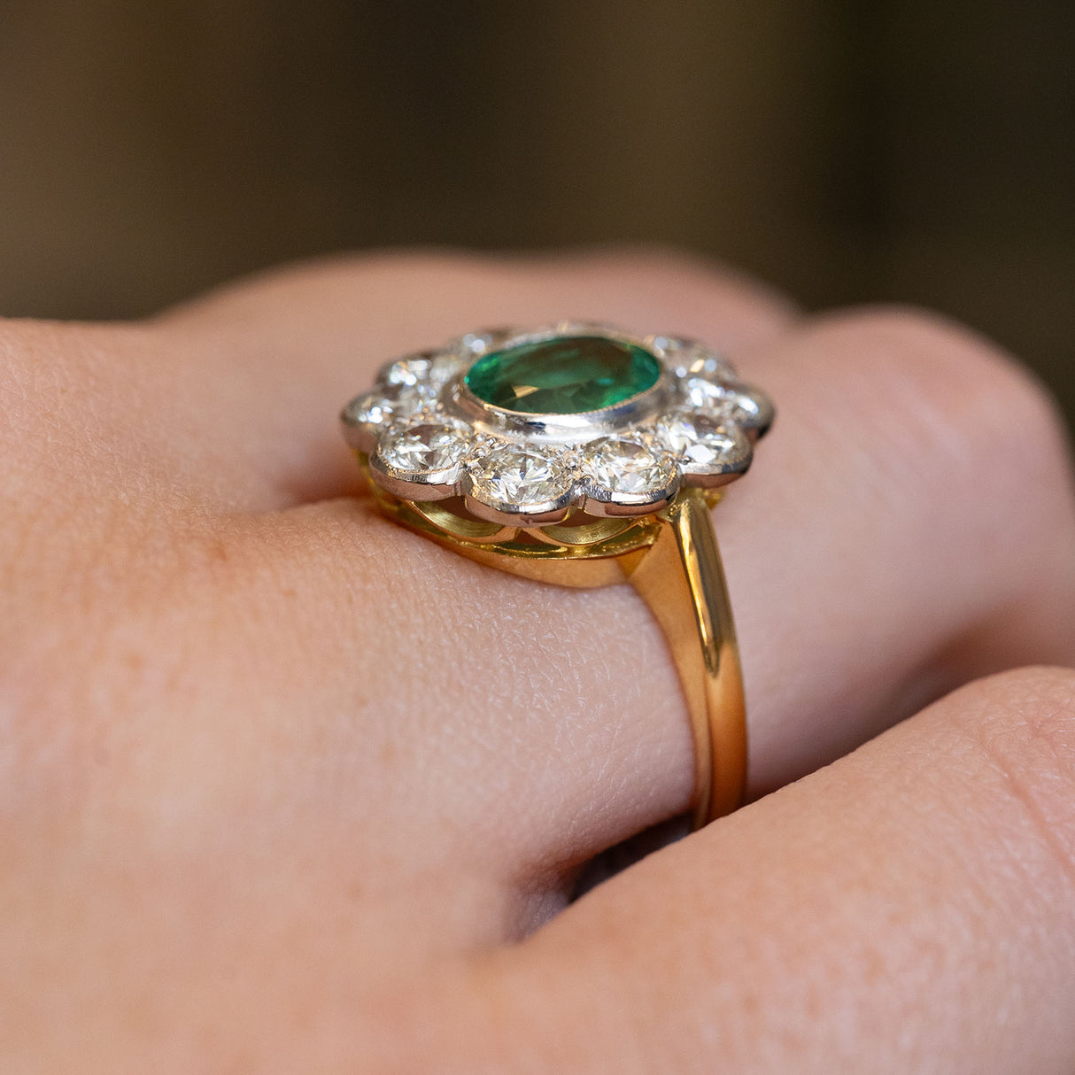 A close-up of a vintage emerald & diamond cluster engagement ring showing the gallery in yellow gold. 