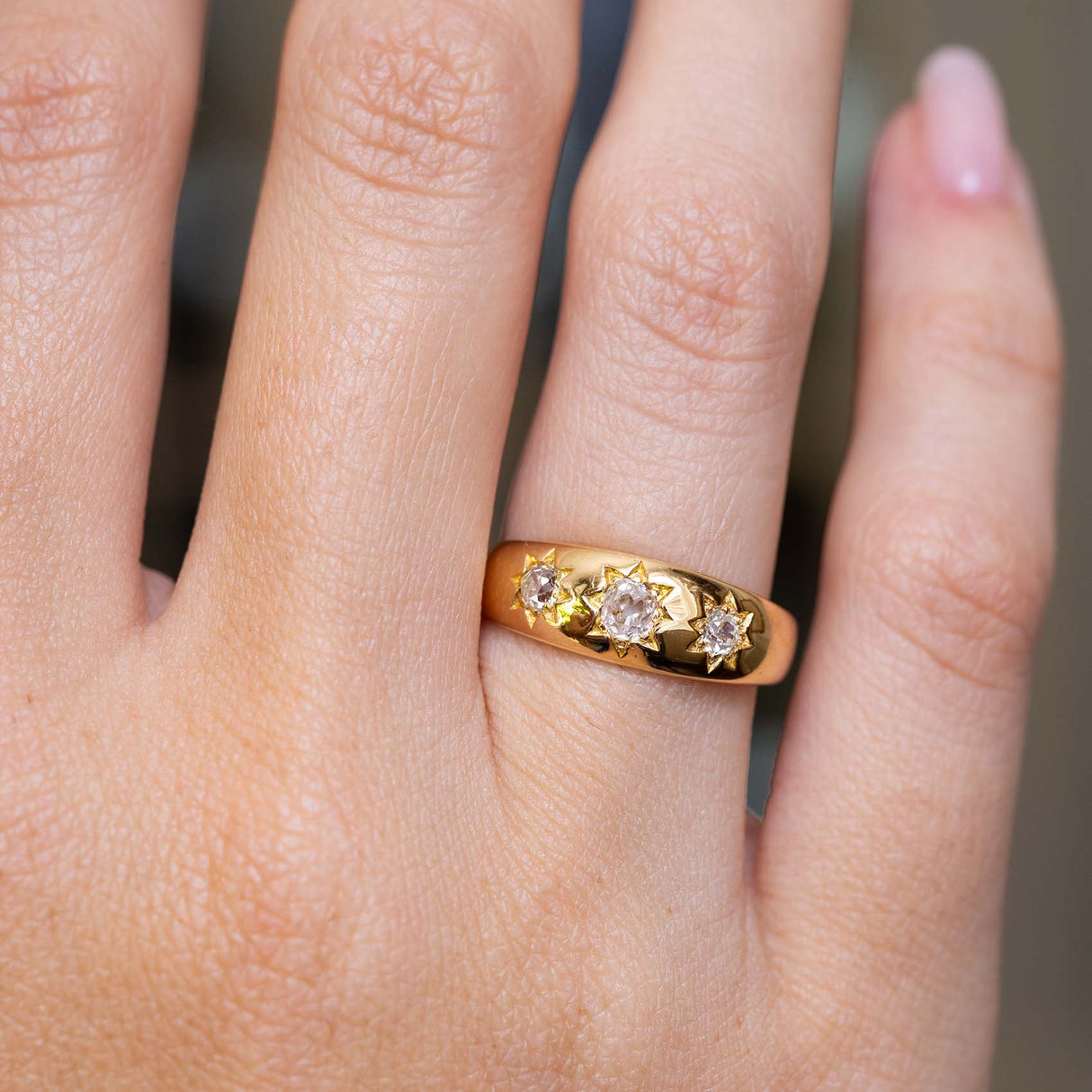 A close-up of a hand wearing a yellow gold ring with three old-mine diamonds. 