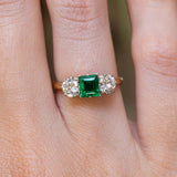 A vintage 1960s emerald and diamond three-stone ring worn on the finger.