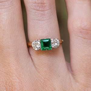 A vintage 1960s emerald and diamond three-stone ring worn on the finger.