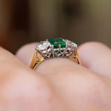 Side detail of a vintage 1960s emerald and diamond three-stone ring worn on the finger.