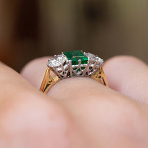 Side detail of a vintage 1960s emerald and diamond three-stone ring worn on the finger.