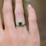 A vintage 1960s emerald and diamond three-stone ring worn on the hand.