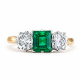 A close-up of a Vintage, 1960s emerald and diamond three-stone ring with a yellow gold band.