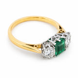 A three-quarter of a vintage, 1960s emerald and diamond three-stone ring with a platinum gallery and yellow gold band.