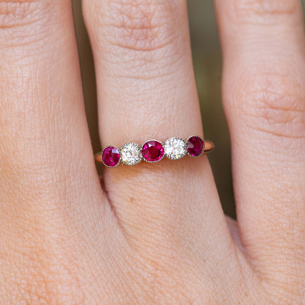 An antique Edwardian ruby and old-cut diamond five-stone ring worn on the finger.