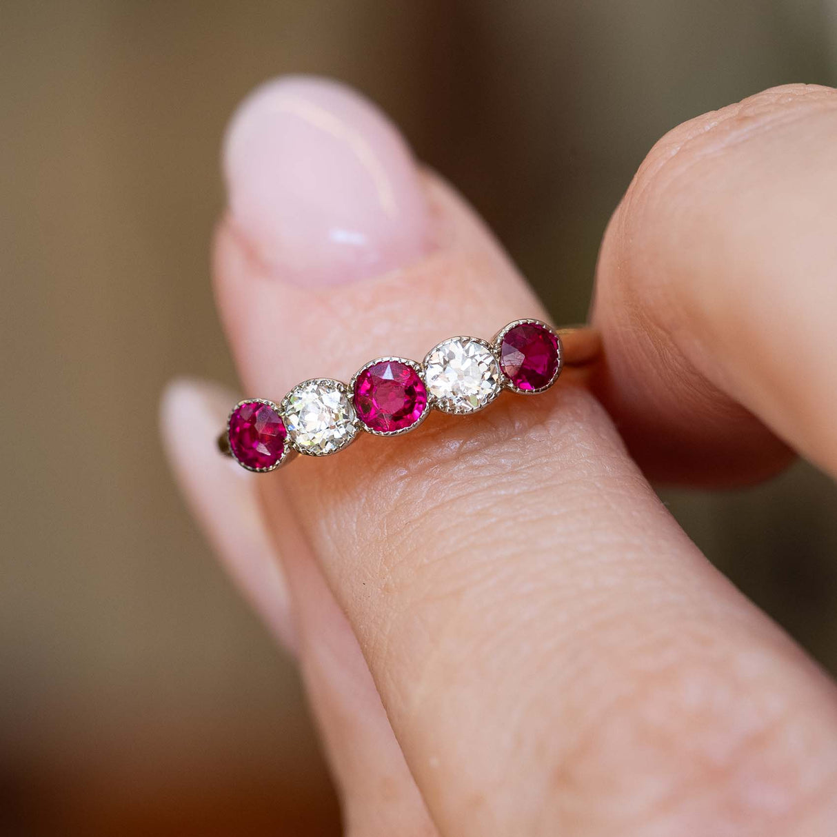 An antique Edwardian ruby and old-cut diamond five-stone ring held between the fingers.