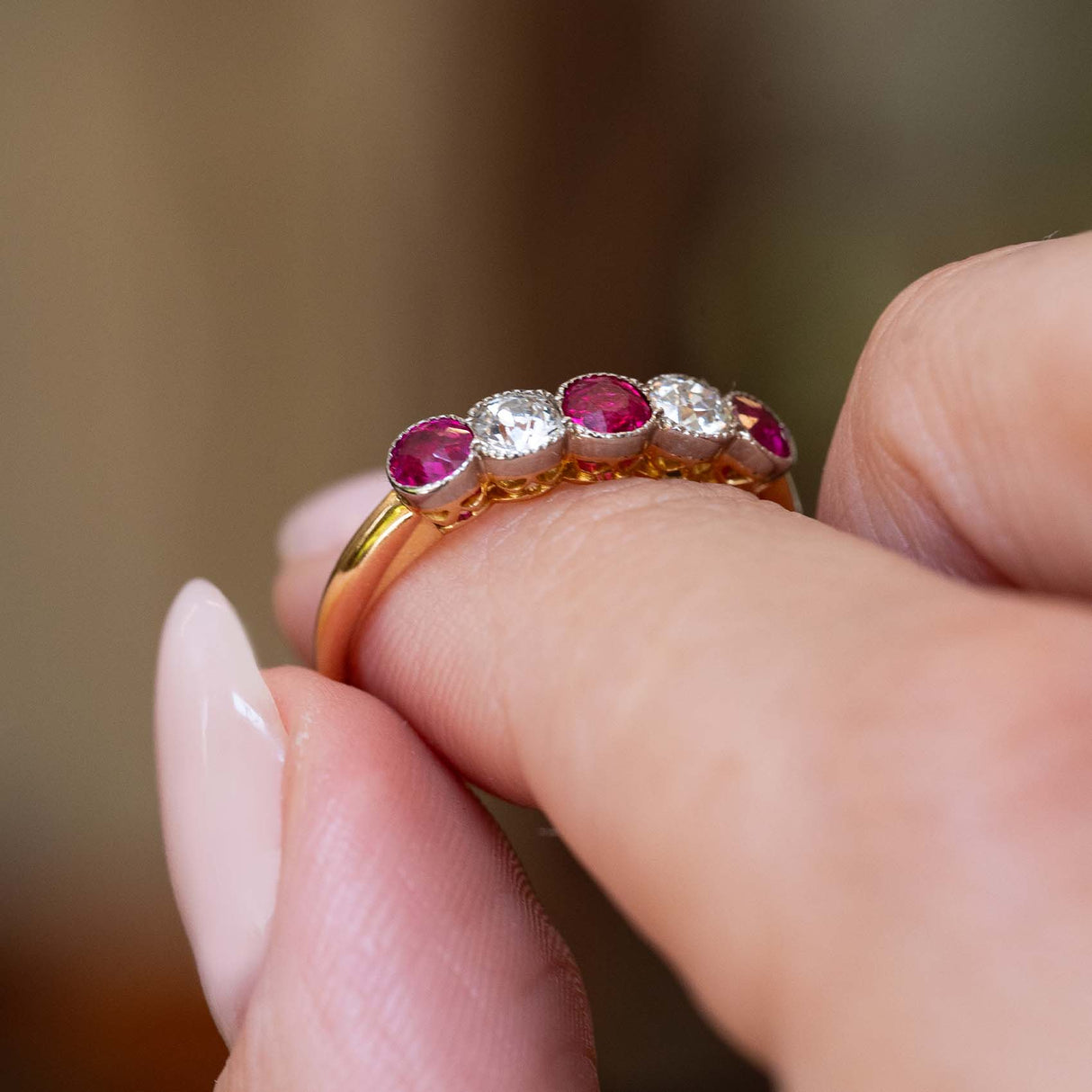 Side detail of an antique Edwardian ruby and old-cut diamond five-stone ring held between the fingers.