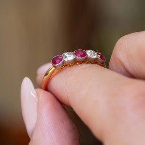 Side detail of an antique Edwardian ruby and old-cut diamond five-stone ring held between the fingers.