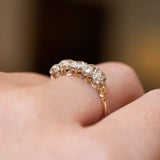 A close-up of a gold ring with silver claws and five diamonds set in a row, worn on a person's finger showing the side profile of the setting. 