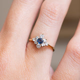 A close-up of a hand wearing vintage, 1990s sapphire & diamond cluster ring with a yellow gold band.