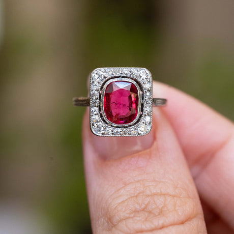 An antique Art Deco red spinel and diamond cluster ring held between the fingers.