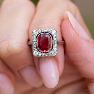 Front detail of an antique Art Deco red spinel and diamond cluster ring held between the fingers.