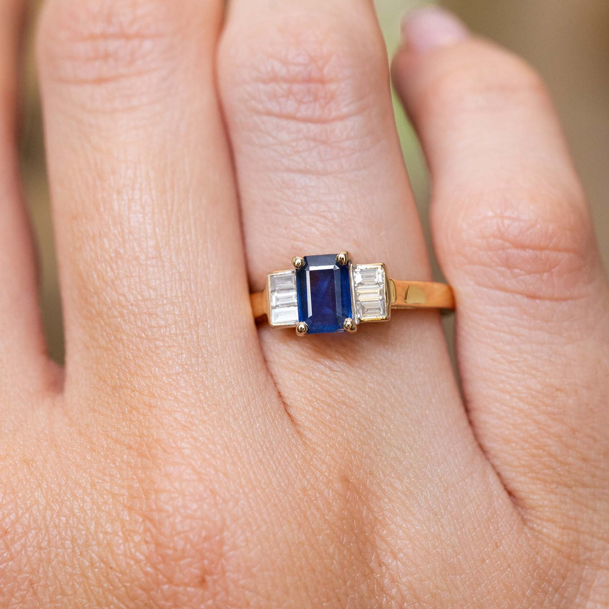 Close-up of a blue sapphire and baguette diamond three-stone ring on the finger