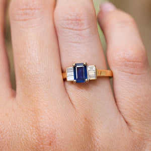 Close-up of a blue sapphire and baguette diamond three-stone ring on the finger
