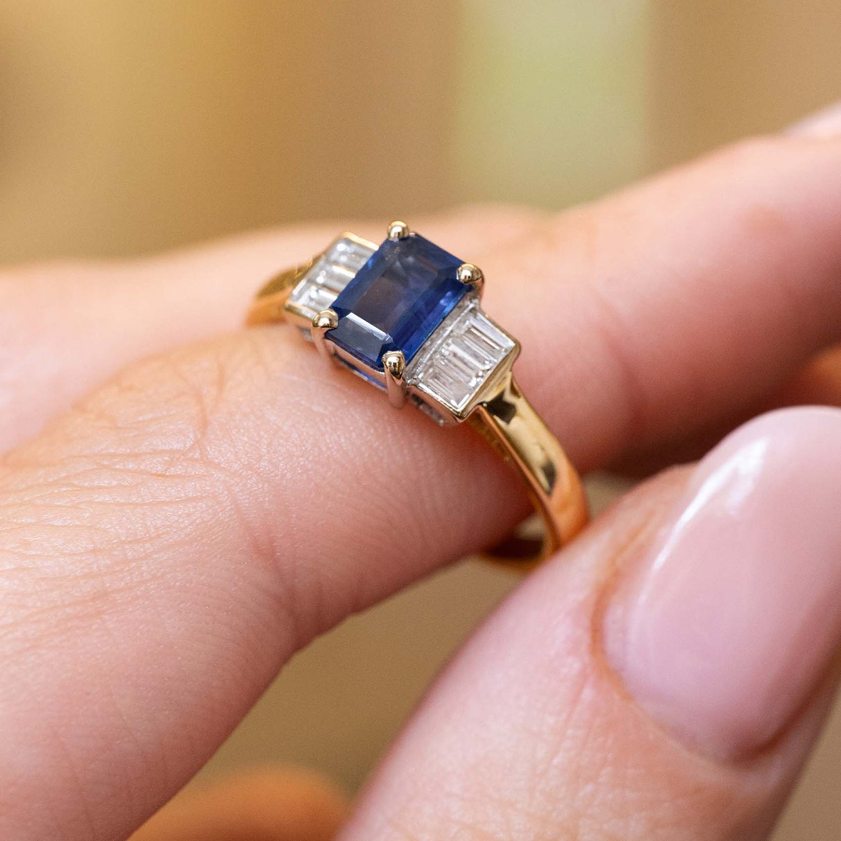 Vintage sapphire and diamond three-stone ring held between the fingers.
