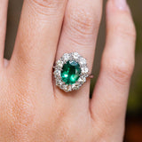 Vintage 1950s oval-cut emerald and diamond cluster engagement ring in white gold worn on the finger.