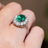 Close detail of a vintage 1950s emerald and diamond halo cluster engagement ring in white gold.