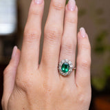 Vintage 1950s oval-cut emerald and diamond engagement ring showcased on the hand in white gold.