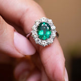 Oval-cut emerald surrounded by a diamond cluster in a vintage 1950s white gold engagement ring.