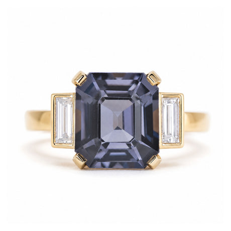 A close-up of a vintage-inspired, Blue spinel and diamond three-stone engagement ring in 14ct yellow gold.