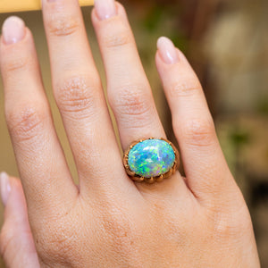 A view of a vintage 1970s cabochon Australian opal ring worn on a hand with a blurred background.