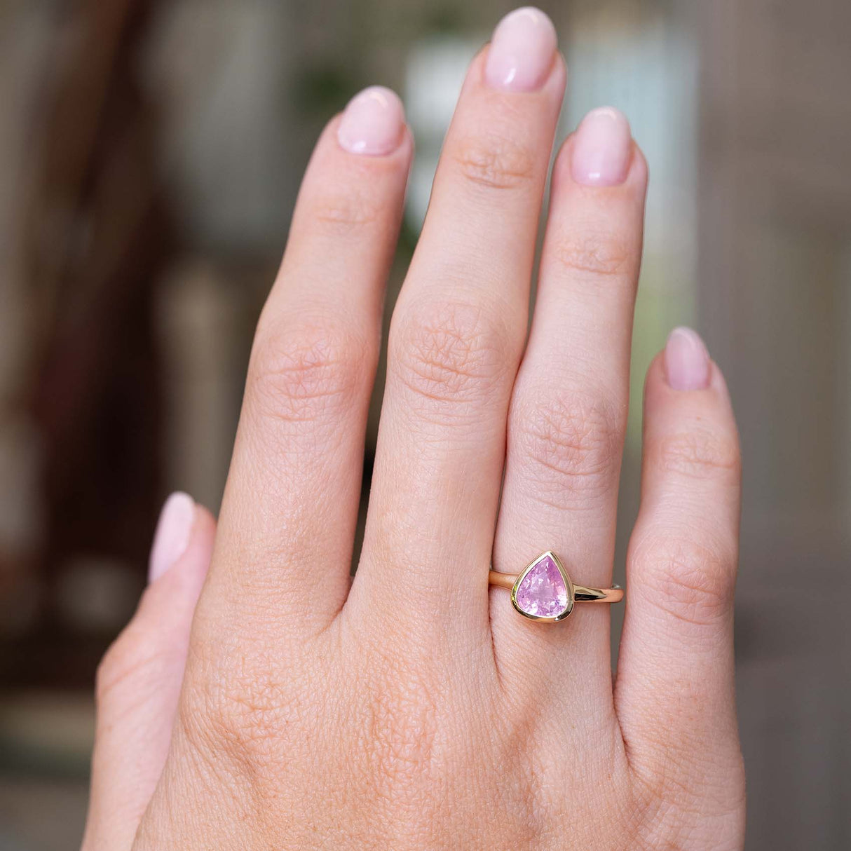 An image of a hand wearing an Antique-inspired, drop shaped light pink sapphire solitaire engagement ring in yellow gold seen from a distance to display the proportions of the ring.