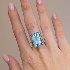 Vintage 1970s aquamarine and diamond cocktail ring worn on a hand, displaying its striking rectangular blue gemstone and polished white gold band.