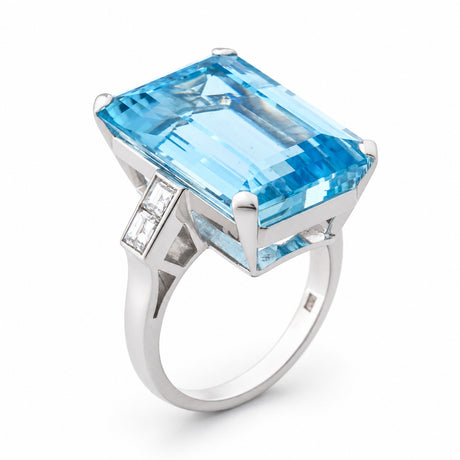 Angled view of a vintage 1970s aquamarine cocktail ring in white gold, showcasing its emerald-cut aquamarine, baguette-cut diamond shoulders and geometric setting.