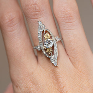 Close-up of an antique Art Nouveau diamond ring on the finger, featuring a central old-cut diamond framed by sweeping platinum and yellow gold details.