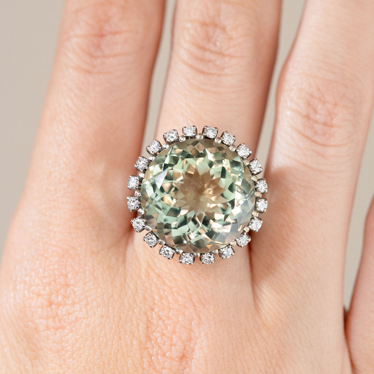Close-up of the white gold cocktail ring on a finger, highlighting the faceted green quartz and brilliant diamond border.