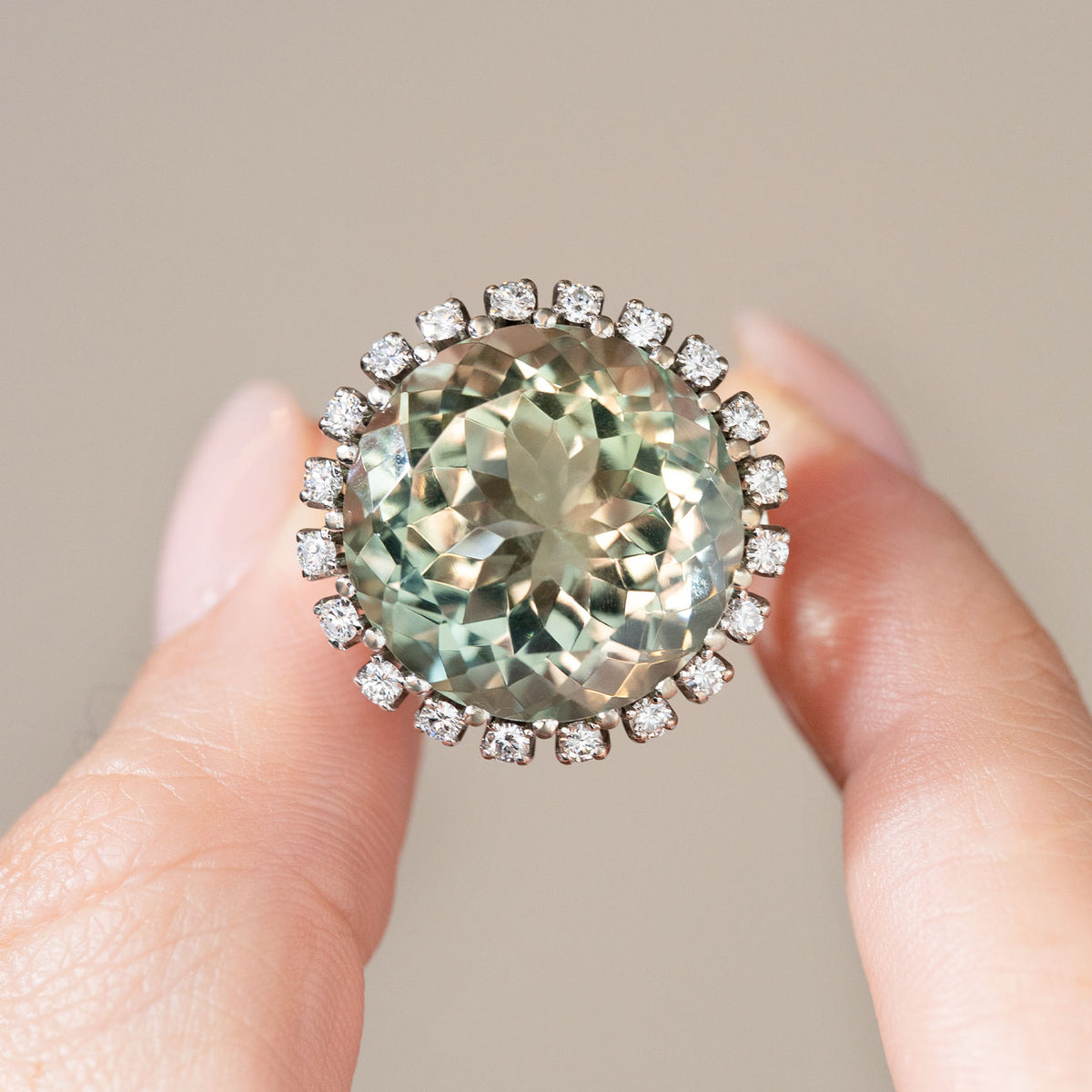 Detailed photograph of the green quartz and diamond ring held between fingers, highlighting its pale sage-green gemstone and surrounding diamonds.