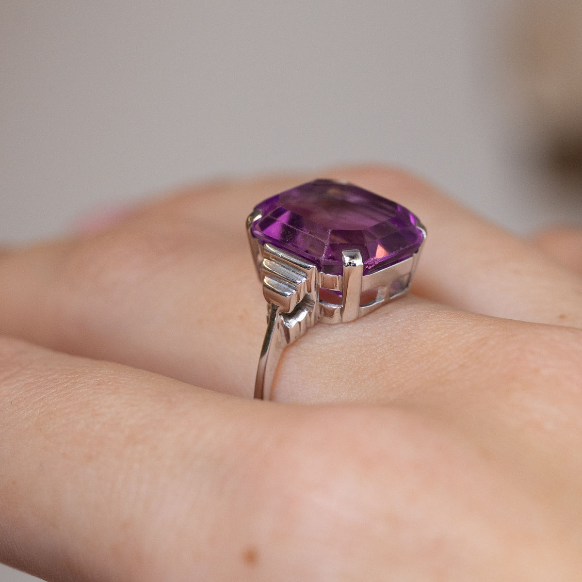 Side-angle view of the antique amethyst ring worn on a finger, revealing the raised gemstone setting and stepped white gold shoulders.