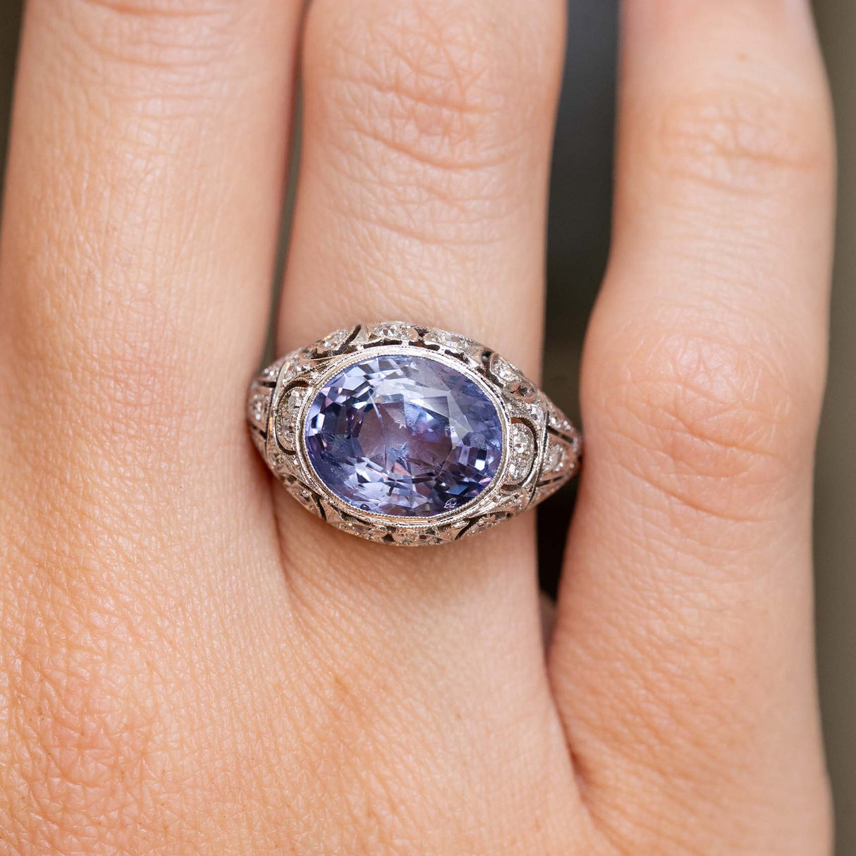 a close up image of an Antique, Belle Époque Ceylon colour-change sapphire and diamond cluster ring in platinum worn on the hand