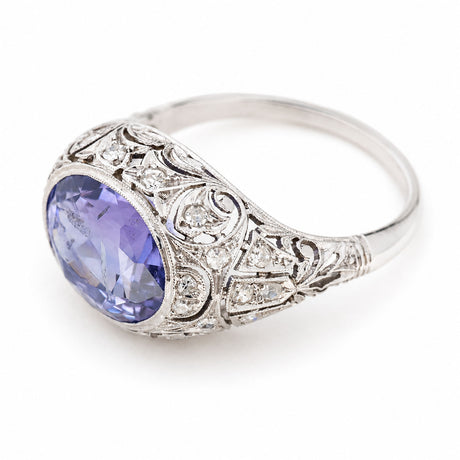 Antique, Belle Époque Ceylon colour-change sapphire and diamond cluster ring in platinum against a plain white background seen from an angle to show the intricate details of the ring.