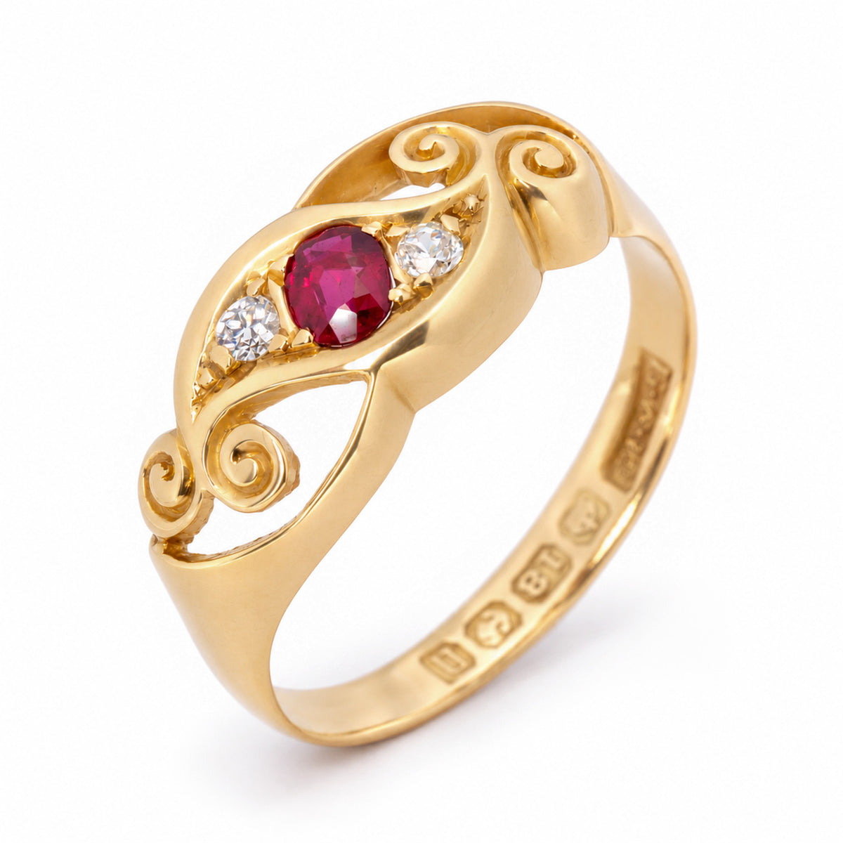 Elevated studio portrait of the Edwardian three-stone ring, revealing its ruby centre, diamond accents and ornate gold scrolls.