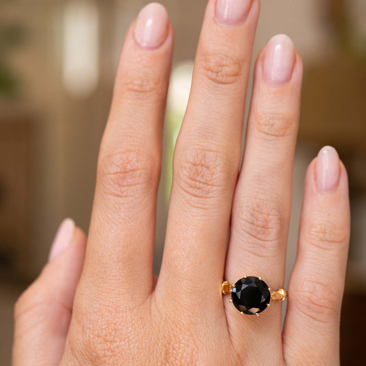 A close-up of a hand wearing a yellow gold Vintage 1980s ring set with a large round dark green tourmaline.