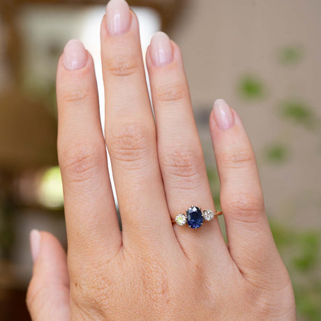A picture of an Antique, Art Deco era blue sapphire and diamond three-stone engagement ring on a yellow gold band worn on an outstretched hand to show the scale of it. 